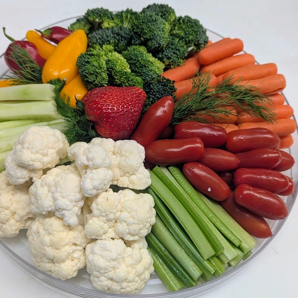 Large platter of fresh vegetables, mini sausages, peppers, herbs, and a strawberry arranged as an appetizer tray.