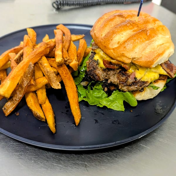 Bacon cheeseburger with lettuce on a toasted bun, served alongside golden fries on a black plate.