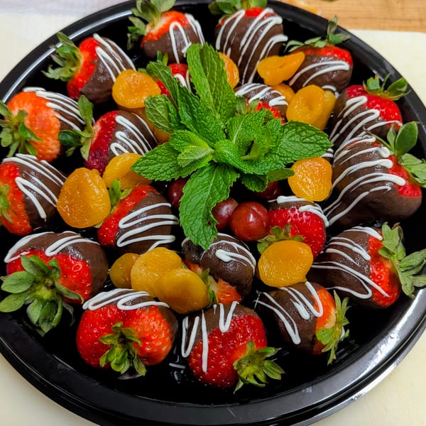 Platter of chocolate-dipped strawberries and apricots drizzled with white chocolate, garnished with fresh mint.
